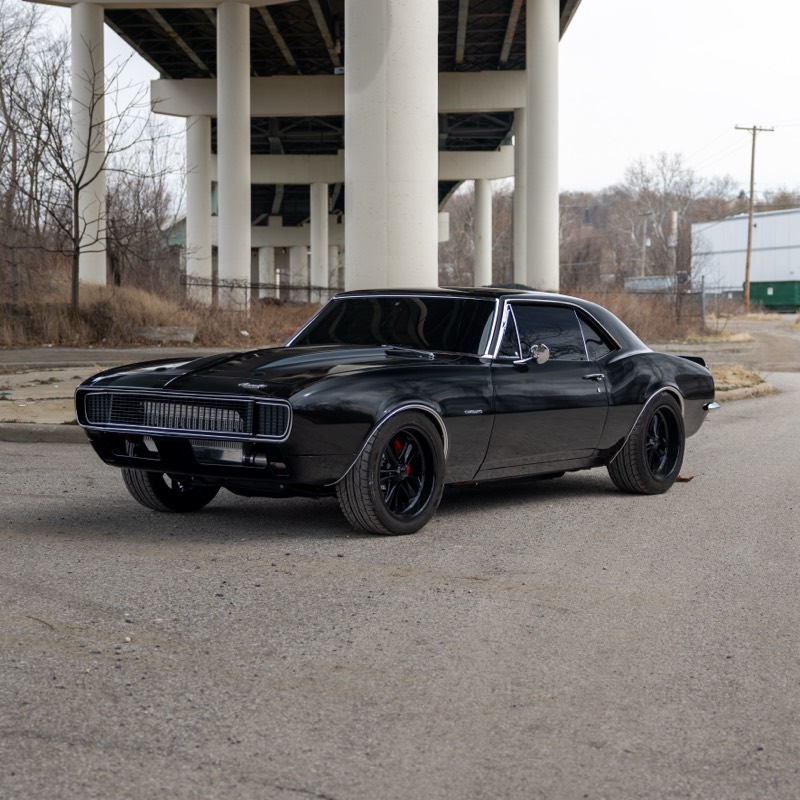 Black 1967 Chevrolet Camaro under a highway overpass, front three-quarter view