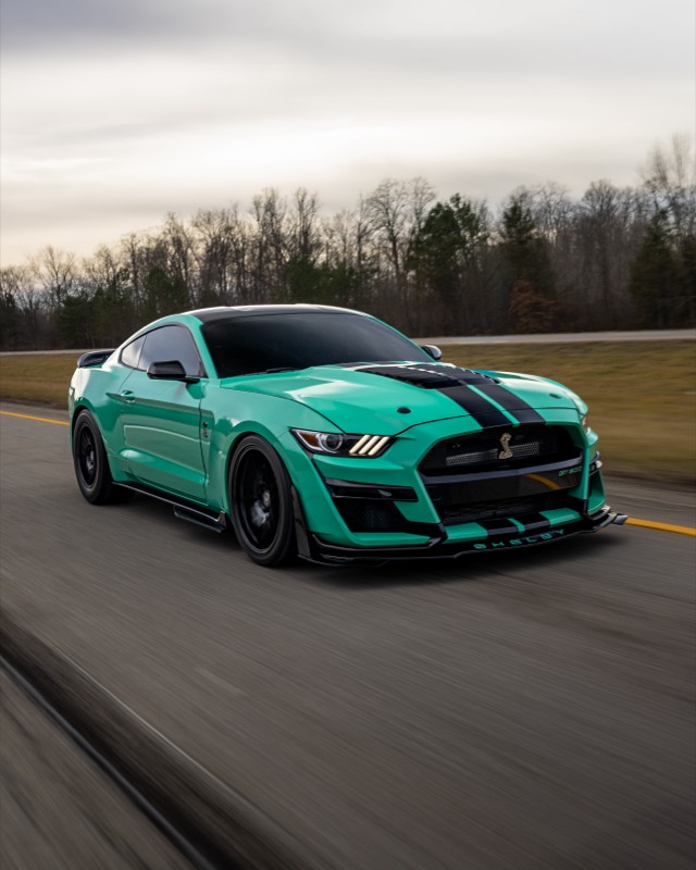 Teal Ford Mustang GT with black stripes, driving on a road